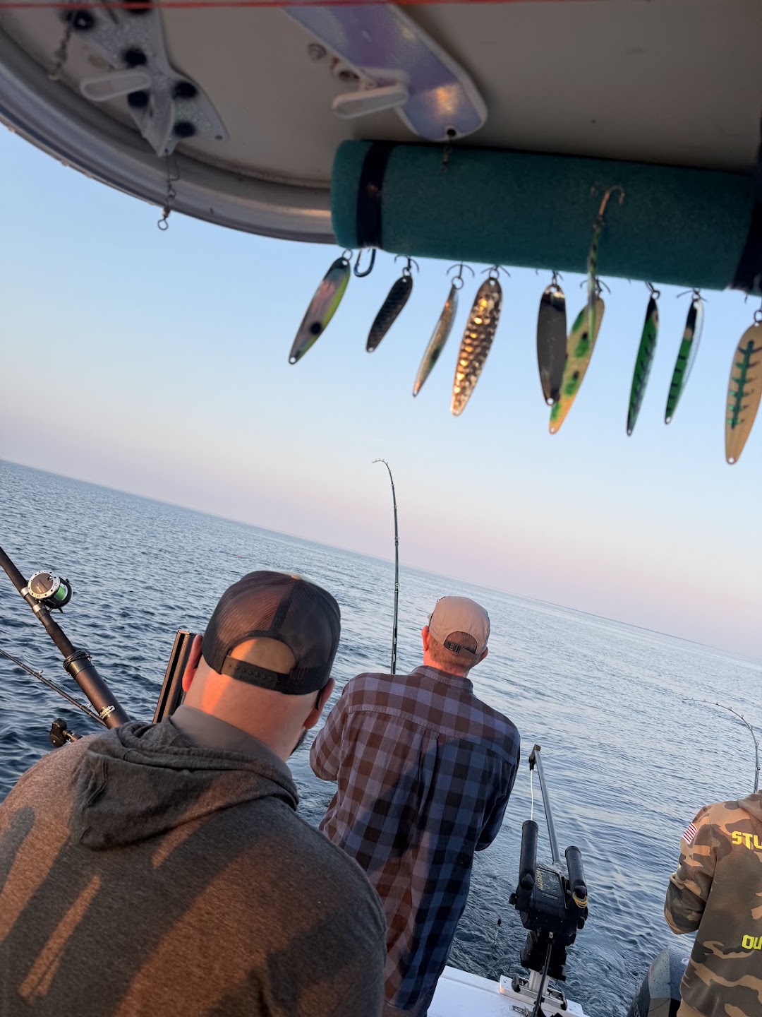 Charter spoons hanging above the deck while two anglers watch their rods on Lake Michigan