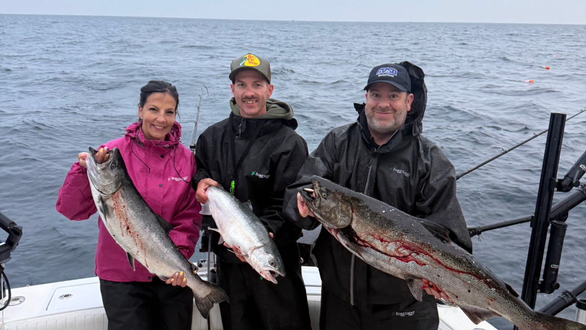 Three guests in rain gear holding king and coho salmon on the charter boat on Lake Michigan